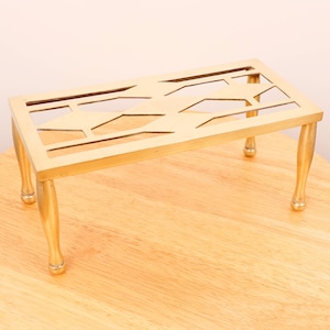 Può includere: Un supporto decorativo in metallo dorato con un design geometrico e quattro gambe. Il supporto è su una superficie in legno.