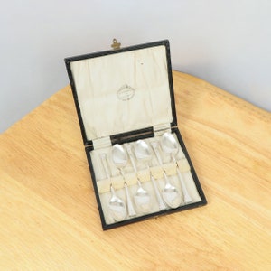 May include: A black velvet box with a silver lining, containing six silver teaspoons. The box is open and the spoons are arranged in rows.