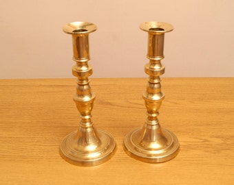 May include: A pair of antique brass candlesticks with a fluted design. The candlesticks are tall and slender, with a flared base.