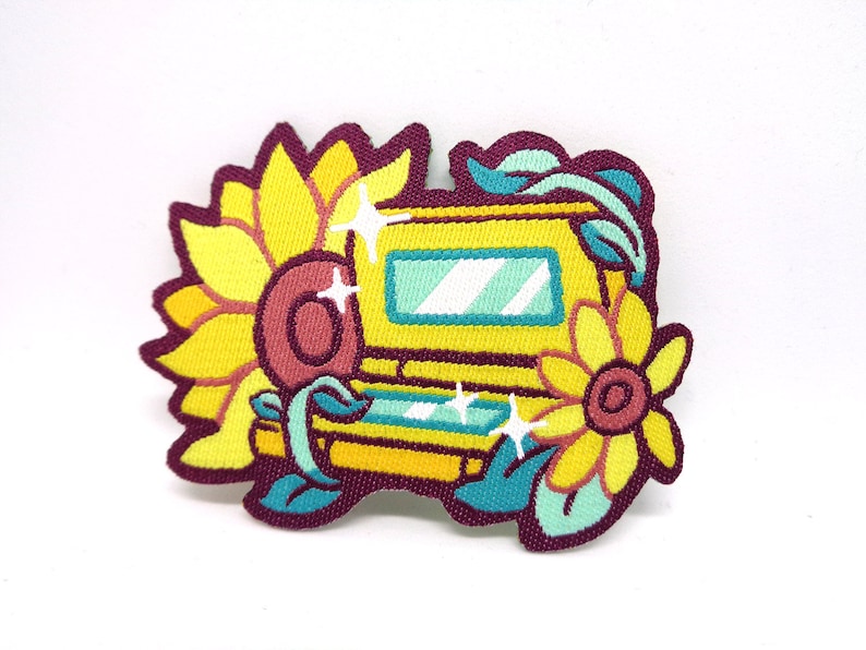 May include: Yellow embroidered patch with a yellow and green game console surrounded by sunflowers and leaves. The console has a blue screen and a pink button.