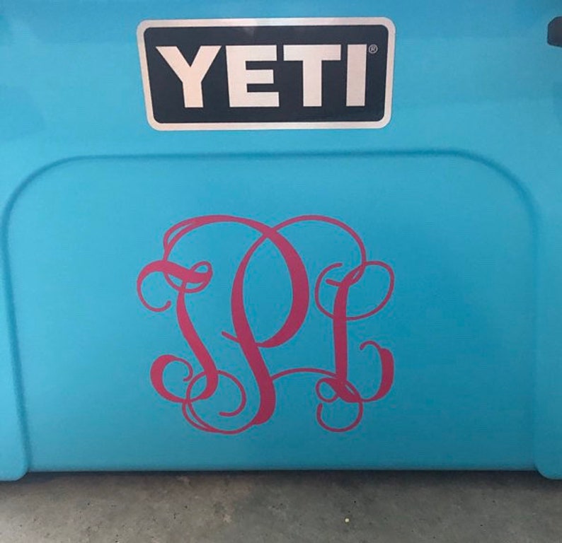 Puede incluir: Una nevera Yeti azul con un monograma rosa de las letras "PL" en la parte delantera.