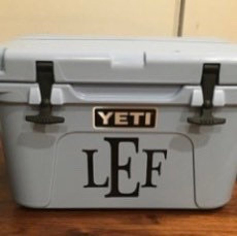 Puede incluir: Una nevera Yeti azul claro con un monograma negro "LEF" en la parte delantera.