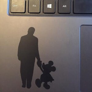 Puede incluir: Silueta negra de un hombre sosteniendo la mano de Mickey Mouse. La silueta está en una computadora portátil plateada.