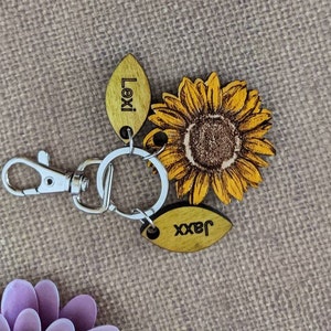 May include: A wooden keychain with a sunflower design and two wooden tags. The tags are engraved with the names "Lexi" and "Jaxx".
