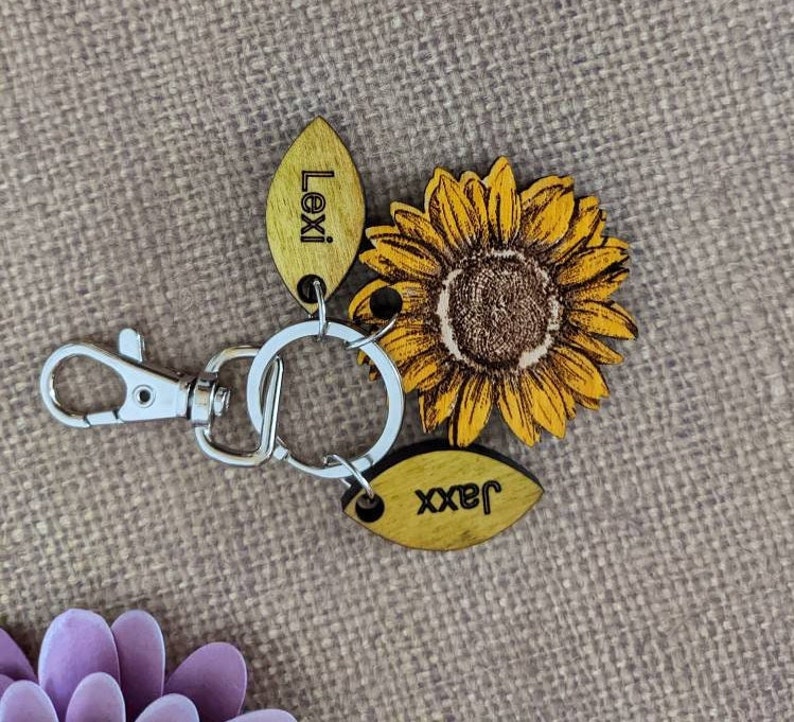 May include: A wooden keychain with a sunflower design and two wooden tags. The tags are engraved with the names "Lexi" and "Jaxx".