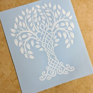 May include: A white vinyl decal of a Celtic knot tree design. The tree has a thick trunk with intricate knots and branches that spread out into a leafy crown.