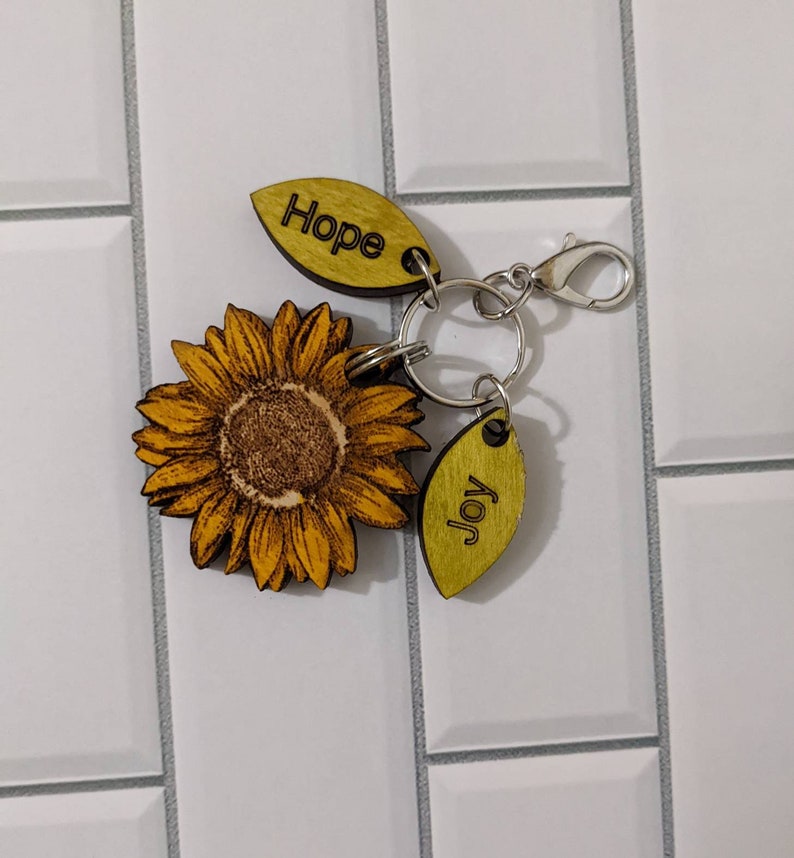 May include: A wooden sunflower keychain with a silver key ring and two wooden tags that say "Hope" and "Joy".