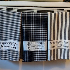 Puede incluir: Tres toallas de cocina con patrones de cuadros y rayas en blanco y negro. Las toallas tienen texto bordado, incluyendo "Boogie-Woogie Bugle Boy", "Murtagh Never leave home without him" y "Murtagh Fitzgibbons Fraser Loyalty Honor Protection".