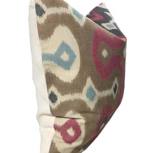 May include: A brown, cream, pink, and blue patterned throw pillow with a white border.