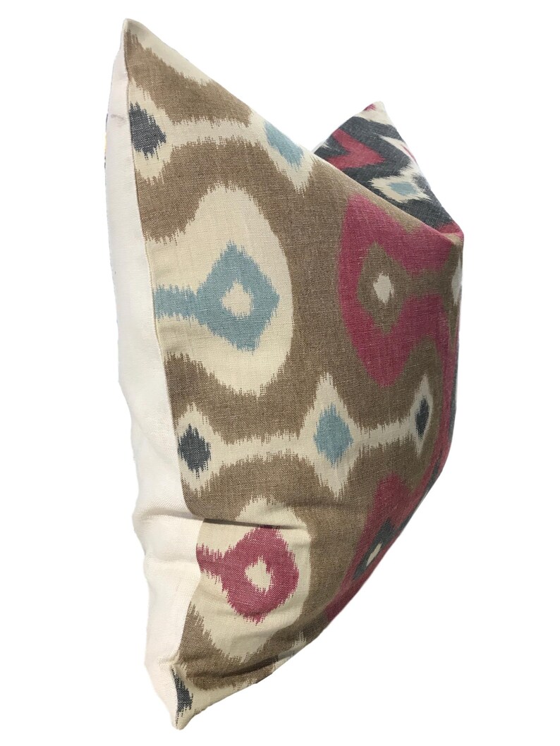 May include: A brown, cream, pink, and blue patterned throw pillow with a white border.