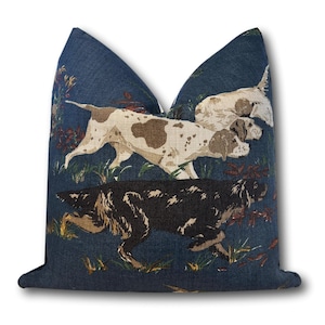 May include: Square throw pillow with a navy blue background featuring a hunting dog design. The dogs are depicted in shades of brown, white, and black, set against a backdrop of foliage.