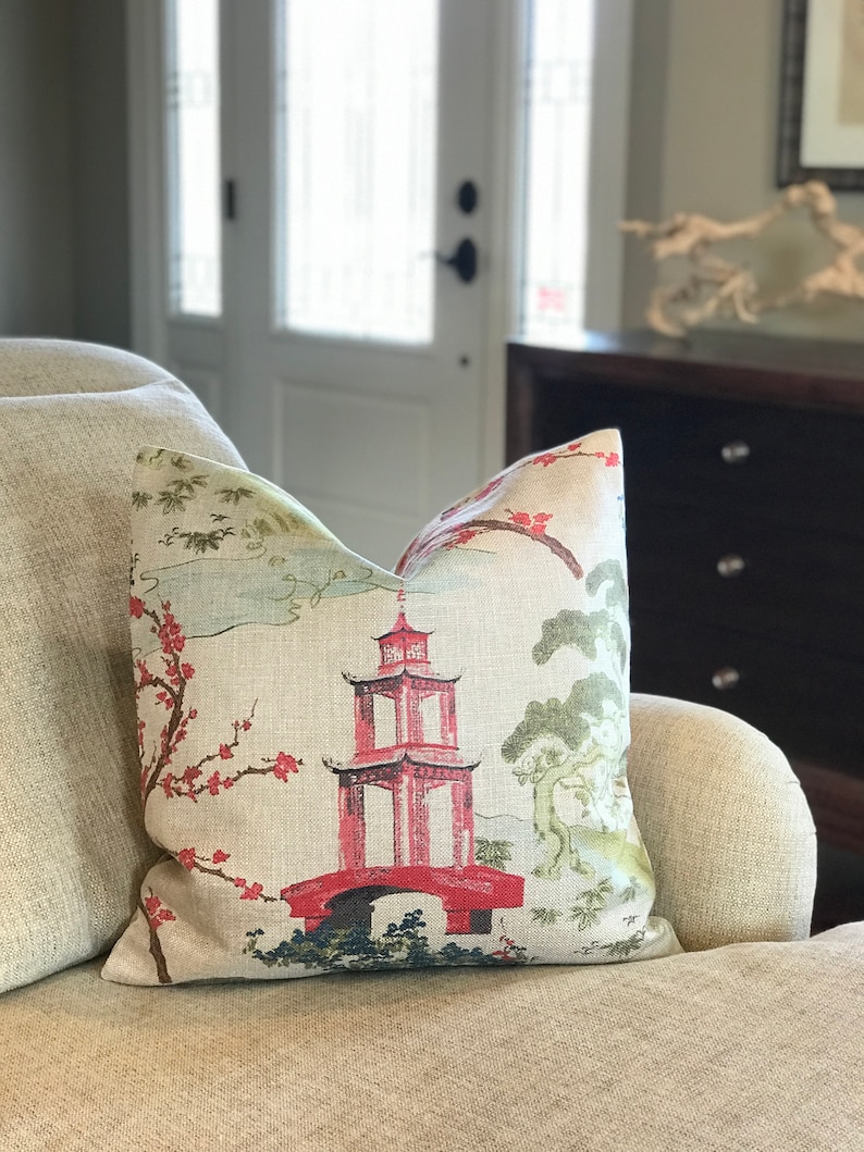 Pode incluir: Uma almofada decorativa com tecido de linho bege que apresenta uma pagoda vermelha e uma ponte com um design floral em tons de rosa, verde e azul.