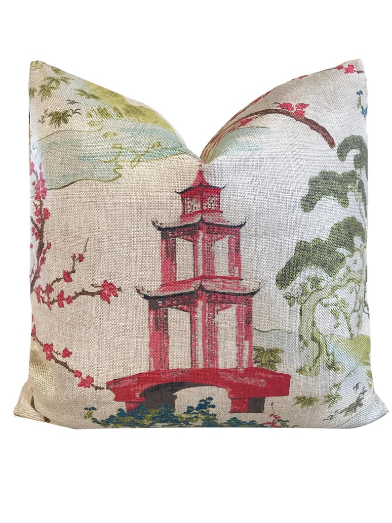 Pode incluir: Uma almofada decorativa com um fundo de linho bege que apresenta uma pagoda vermelha com uma ponte, rodeada de desenhos florais verdes e rosas.