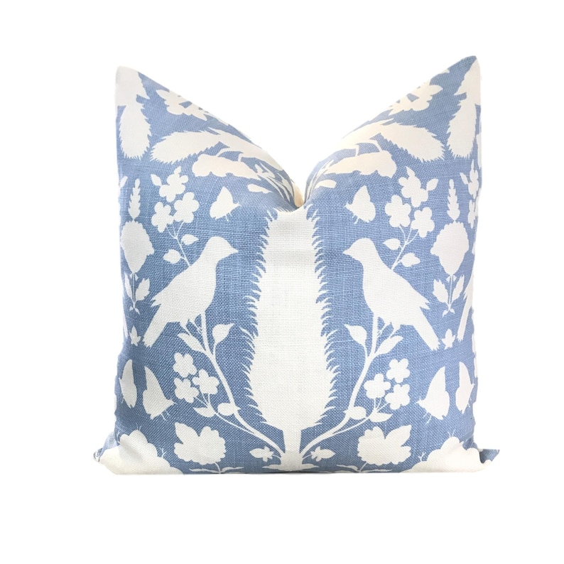 May include: A blue throw pillow with a white floral and bird design. The pillow is made of a soft, textured fabric.