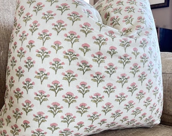 May include: A decorative pillow with a white background and a repeating pattern of pink floral designs. The pillow is placed on a beige sofa, creating a cozy and inviting aesthetic. The floral pattern adds a touch of elegance.