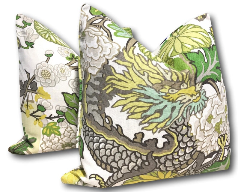 May include: Two decorative throw pillows with a white background and a floral pattern. One pillow features a green and yellow dragon design, while the other pillow features a more subtle floral pattern with green and yellow accents.