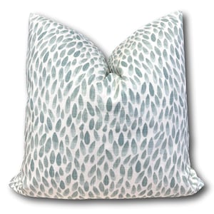 May include: Square decorative pillow with a white background and a pattern of blue-green teardrop shapes. The pillow has a soft, textured appearance, suitable for home decor.