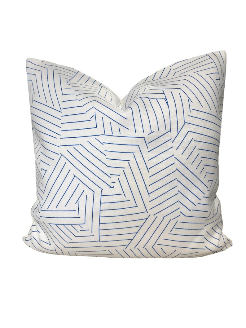 Puede incluir: Almohada blanca con un patr&oacute;n geom&eacute;trico azul de l&iacute;neas que forman formas abstractas.