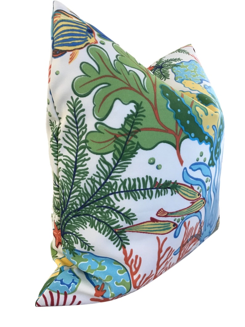 Puede incluir: Una almohada blanca con una escena submarina colorida que presenta algas verdes, coral rojo, peces azules y amarillos y burbujas blancas.