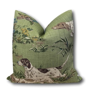 May include: Green decorative throw pillow with a repeating pattern of dogs, birds, and foliage. The dogs are brown and white, and the birds have blue and brown accents. The pillow has a textured appearance.