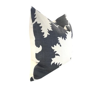 K&ouml;nnte beinhalten: Ein quadratisches Zierkissen mit einem wei&szlig;en, stilisierten Blumenmuster auf marineblauem Hintergrund. Das Kissen ist wahrscheinlich aus einem strukturierten Stoff gefertigt, was dem Design visuelles Interesse verleiht.