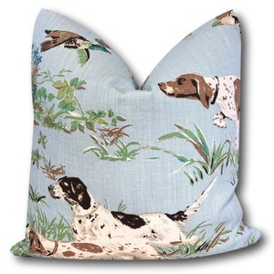May include: A light blue throw pillow with a hunting dog and duck pattern. The pillow features a white background with brown, black, and green accents.