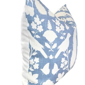 May include: A blue pillow with a white floral and bird design. The pillow is made of a soft, textured fabric.