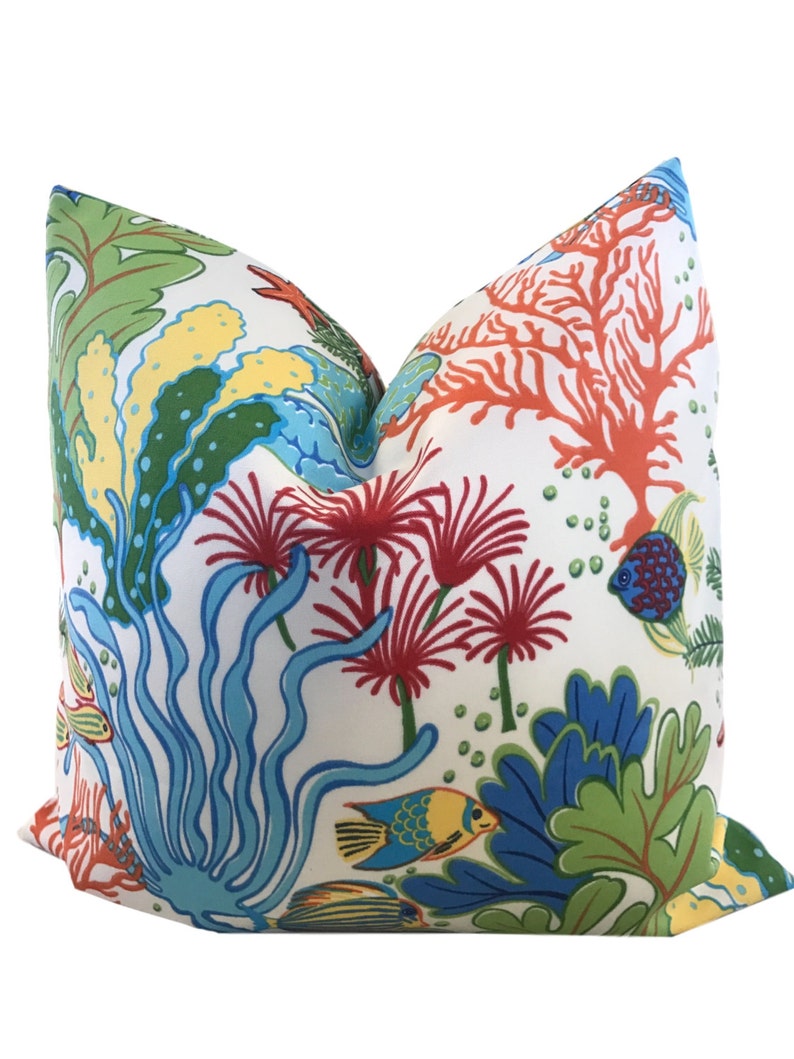 Puede incluir: Una almohada blanca con un dise&ntilde;o de arrecife de coral colorido. La almohada presenta corales, peces y algas rojas, naranjas, azules, verdes y amarillas.