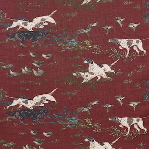 May include: A red fabric with a repeating pattern of white and brown dogs running through a field of green grass and blue flowers.  There are also small brown birds flying in the air.