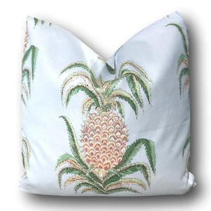 May include: A light blue pillow with a pineapple pattern. The pineapple is surrounded by green leaves and has a brown and yellow body with pink accents.