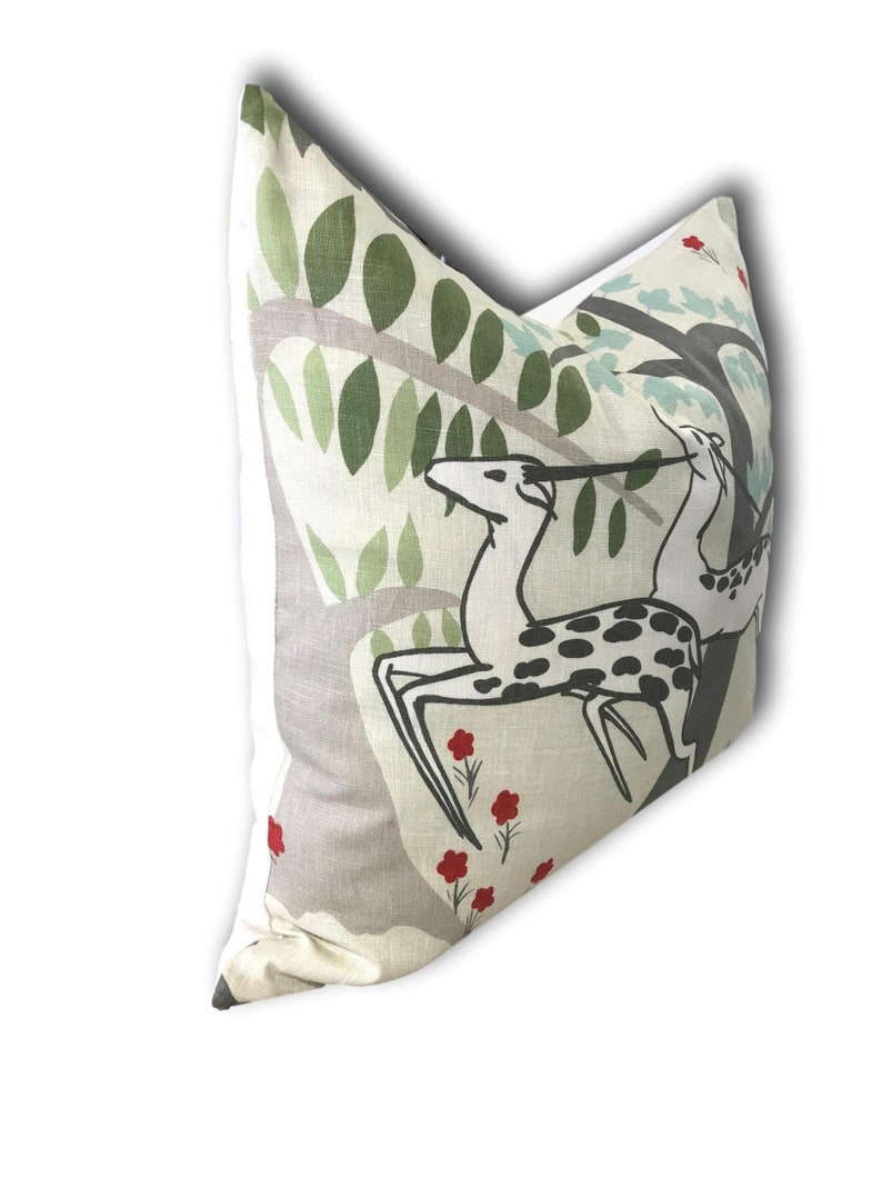 May include: A beige pillow with a white border features a stylized illustration of two deer in a forest setting. The deer are black and white with red flowers scattered throughout the design.