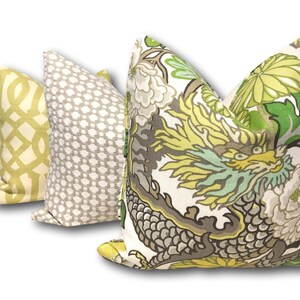 May include: Three decorative throw pillows with different patterns. The first pillow is a light yellow with a white geometric pattern. The second pillow is a light gray with a white geometric pattern. The third pillow is white with a green, yellow, and gray dragon and floral pattern.