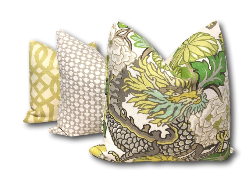 May include: Three decorative throw pillows with different patterns. The first pillow is a light yellow with a white geometric pattern. The second pillow is a light gray with a white geometric pattern. The third pillow is white with a green, yellow, and gray dragon and floral pattern.