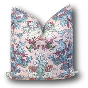 May include: A pink pillow with a blue and green dragon design. The pillow has a white border and is made of a soft, textured fabric.
