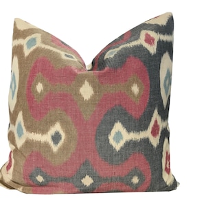 May include: A decorative pillow with a geometric pattern in shades of red, brown, blue, and white. The pillow has a soft, textured fabric and a subtle sheen.