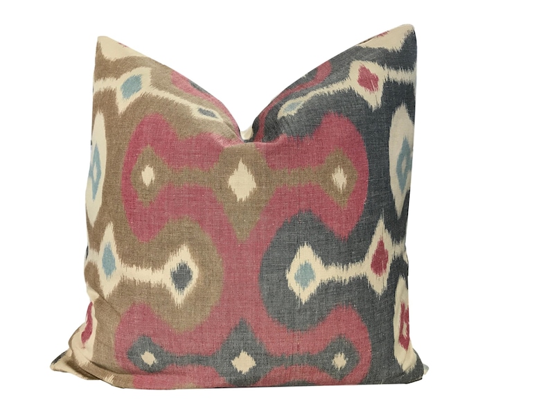 May include: A decorative pillow with a geometric pattern in shades of red, brown, blue, and white. The pillow has a soft, textured fabric and a subtle sheen.