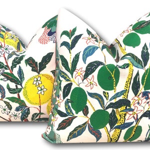 May include: Two decorative throw pillows with a botanical design. The pillows feature a white background with a pattern of green leaves, yellow citrus fruits, and white and red flowers. The design is repeated on both pillows.
