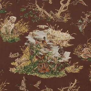 May include: Brown fabric with a hunting scene featuring a dog, ducks, and a stream. The design includes trees, tall grass, and a woven basket, creating a rustic, outdoorsy aesthetic. The fabric is suitable for upholstery or crafting.