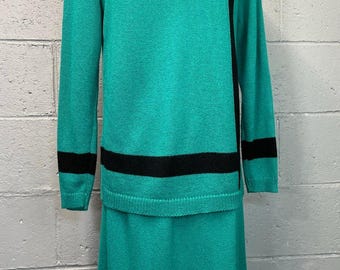 May include: A teal two-piece knit set. The long-sleeved top has a black neckline and a black stripe on the sleeves. A black vertical stripe runs down the left side. The matching skirt is knee-length.