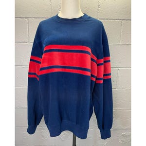 May include: A navy blue sweatshirt with red and navy blue striped detail across the chest and sleeves.