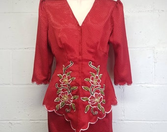 May include: A red dress with a scalloped hem and floral embroidery. The dress has a fitted bodice and a full skirt.