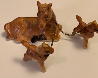May include: A ceramic horse figurine set featuring a resting mother horse and two foals connected by a chain. The horses are brown with black accents and a glossy finish. A vintage-style decorative piece.