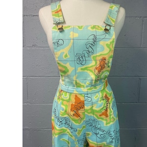 May include: A vintage jumpsuit with a map-like design in shades of blue, yellow, and orange. The jumpsuit features adjustable straps with metal ring hardware. The fabric is printed with the words "Paradise Ocean" and other text.