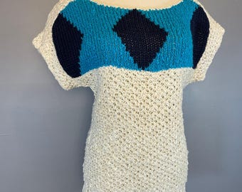 May include: Cream-colored knit top with a scoop neck and short sleeves. The top features a blue and navy blue geometric design across the chest. The body of the top has an open weave pattern.