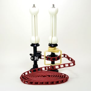 May include: Two white and black camera support stands with a red track system. The stands have a screw top and a black base. The track system is a series of red rectangular links.
