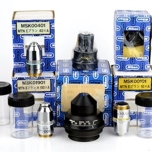 May include: A collection of microscope objectives and boxes, including a 100x objective, a 40x objective, a 10x objective, and a black objective with a rotating dial. The boxes are blue and white with the Nikon logo and the text "MTN Eプラン" and the magnification.