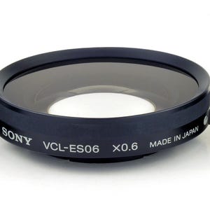 May include: Three black camera lens accessories on a white background. The center lens is labeled "SONY VCL-ES06 X0.6 MADE IN JAPAN". The accessories include a lens, a ring, and an adapter.