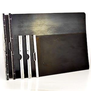 May include: A set of dark gray metal drafting boards with silver metal support arms and handles. The boards are rectangular with rounded corners and show signs of wear. The support arms are designed to hold the boards at an angle.