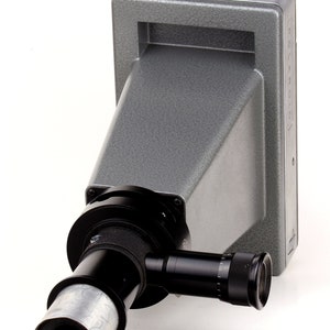 Może przedstawiać: Szary aparat Polaroid Land z czarnym obiektywem i czarnym i srebrnym mieszkiem. Aparat jest przeznaczony do użytku z mikroskopem.