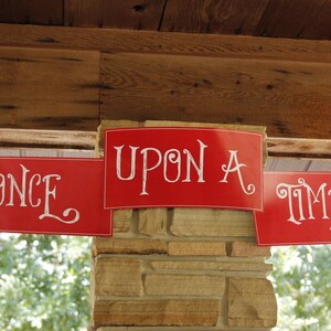 May include: Three red banners with white lettering hang from a wooden ceiling. The banners read "Once", "Upon A", and "Time".